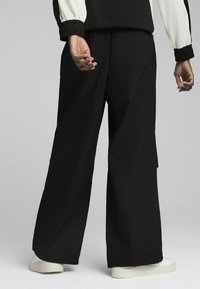 Wide-leg black pants with a high waistband, made from lightweight fabric, featuring a slight shine and cut pockets at the sides.