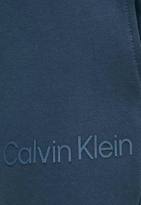 Tela azul marino con una textura suave presenta un logo de Calvin Klein en relieve de un color a juego, situado en el centro.