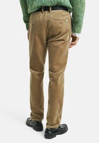 Braune Cordhosen mit glatter Textur und Taschen auf der Rückseite. Kombiniert mit schwarzen Schuhen für einen vollständigen Look.