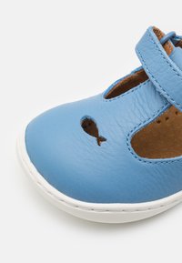 Blauer Lederschuh mit abgerundeter Spitze, perforiertem Fischdesign, verstellbarem Riemen und weißer Gummisohle. Das Innenfutter ist braun.