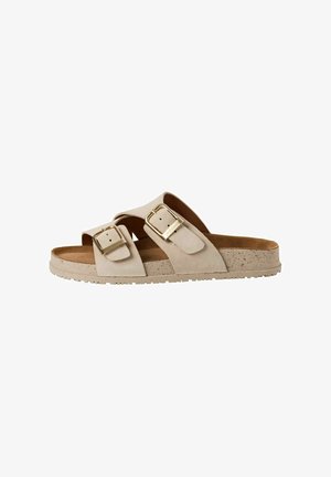 Beige suede sandals with two wide straps, each featuring a gold buckle. Cork-textured sole with a textured rubber outsole.