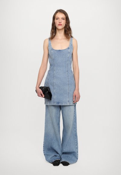 Denim-kleit, millel on ümmargune kaelus, sobiv bodice ja laienev alumine osa, koos vabade laia säärega denimipükstega. Must käekott käes.