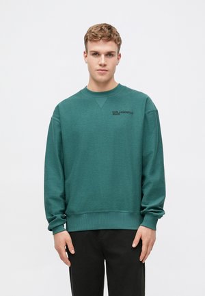 Dunkelgrüner Sweatshirt aus weichem Material, mit einem runden Halsausschnitt und gerippten Bündchen, sowie einem schwarzen Logo auf der Brust.
