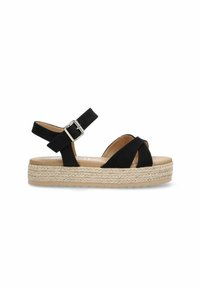 Sandal de ante negro con correas entrelazadas, hebilla en el tobillo y suela de plataforma envuelta en yute. Presenta detalles texturizados y una plantilla de color marrón claro.
