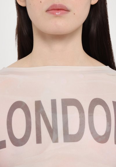 Durchsichtige, hellrosa Bluse mit einem großen, auffälligen "LONDON"-Druck in dunkelgrau. Der Stoff wirkt glatt und leicht durchsichtig.