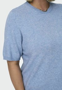 Svetlo modri kratkosleeni pulover iz mehke pletene tkanine. Ponuja okroglo izreznico in rebraste manšete. Tekstura deluje gladko in lahko.