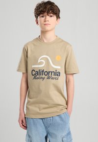 T-shirt di cotone color beige con grafica di un'onda e un sole e la scritta "California Making Waves" in blu navy e nero. Maniche corte, design a girocollo.