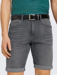 Pantaloncini in denim grigio con orlo risvoltato, dotati di una tasca frontale e una cintura nera con fibbia argento, indossati sopra una camicia verde.
