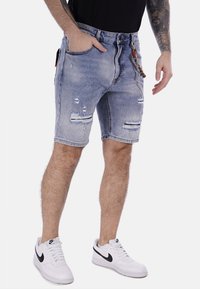 Shorts de mezclilla en azul claro con detalles desgastados. Presentan un ajuste relajado, bolsillos delanteros y un accesorio de llavero decorativo.