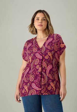 Lila Kurzarm-Oberteil mit einem Paisley-Muster in Pink und Orange, mit V-Ausschnitt und fließendem Design. Kombiniert mit blauer Jeans.