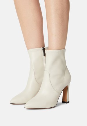 Bottes de cheville en cuir blanc avec un bout pointu, un talon épais et une fermeture éclair arrière. Texture lisse avec des détails de couture minimaux.