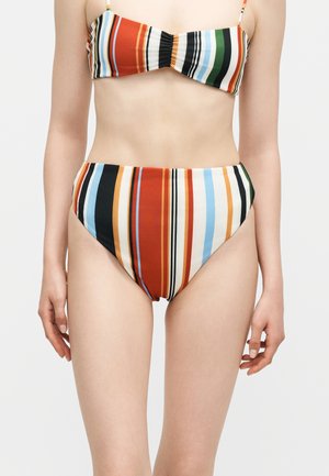 Kobieta nosząca wielokolorowy bikini w pionowe paski z majtkami z wysokim stanem i topem bandeau z cienkimi ramiączkami.