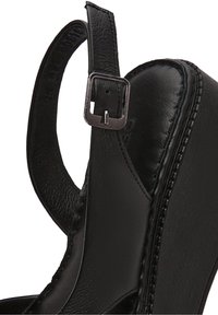 Gros plan sur une sandale compensée en cuir noir avec sangle à boucle ajustable et détails de couture sur la semelle.