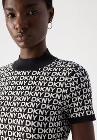 Zwart-wit DKNY gebreide top met patroon, korte mouwen en een geribbelde ronde halslijn. Kenmerkt zich door het herhaalde logo-ontwerp over het gehele oppervlak.