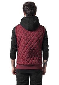 Burgundy vuorattu liivi mustan huppariylihousun kanssa. Liivissä on timanttimallinen kuvio ja ribatt tehdas, joka on yhdistetty teksturoituihin mustiin hihoihin.