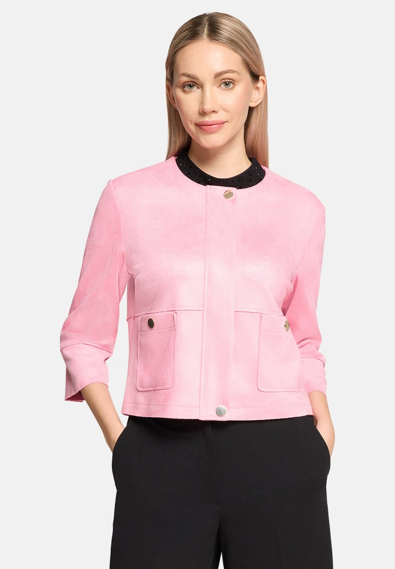 Veste en suede rose avec un col noir rond, des manches trois-quarts, des poches avant avec des boutons-pression en métal, et une texture lisse.