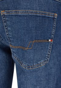 Blue denim jeans with orange stitching, featuring a back pocket embellished with zigzag stitching and a small colored accent in red, white, and blue.