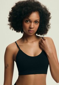 Czarny crop top na cienkich ramiączkach, wykonany z gładkiego, elastycznego materiału. Posiada okrągły dekolt i bezszwową konstrukcję. Tło w odcieniu skóry.