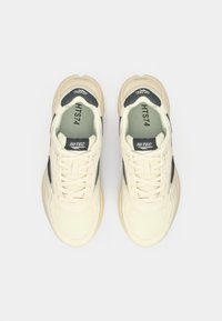 Cream-colored sneakers with a textured mesh upper, contrasting black accents, round toe, and flat laces. Features "HI-TEC" branding and model number.