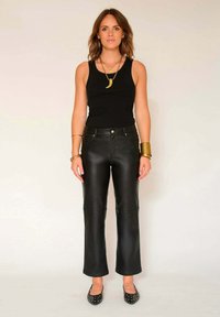 Pantalons en cuir noir au design droit avec des panneaux de genoux cousus, associés à un débardeur noir ajusté et des ballerines noires.