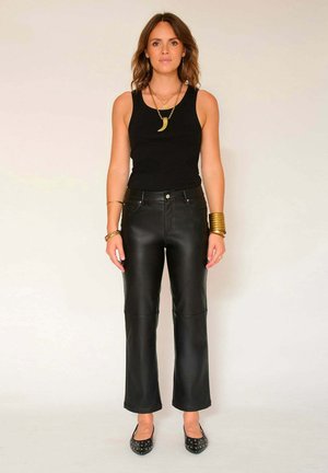 Pantalons en cuir noir au design droit avec des panneaux de genoux cousus, associés à un débardeur noir ajusté et des ballerines noires.