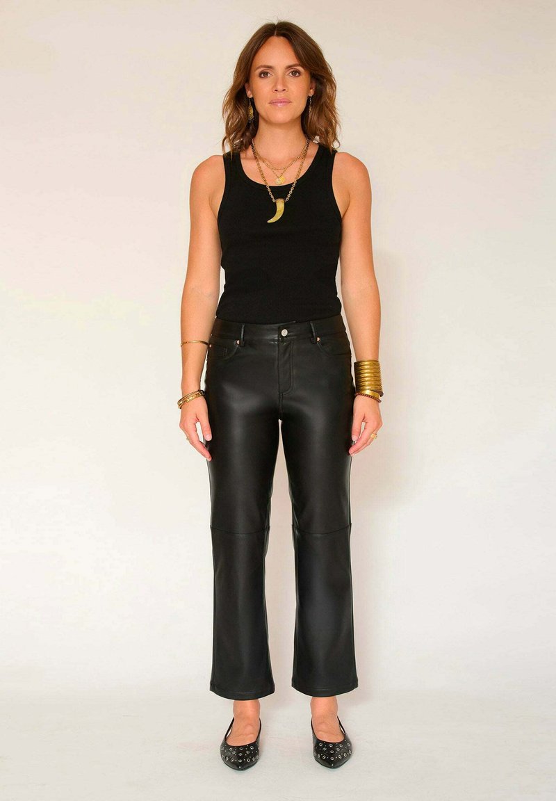 Pantalons en cuir noir au design droit avec des panneaux de genoux cousus, associés à un débardeur noir ajusté et des ballerines noires.