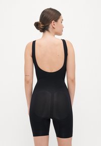 Černý bodysuit s nízkým výstřihem na zádech, úzkými ramínky a šortkami do poloviny stehna. Vyrobeno z hladkého, elastického materiálu s tvarujícími panely pro podporu.