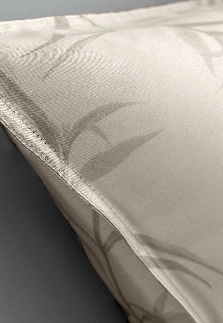 Nahaufnahme eines beigen Stoffs mit zarten grauen Bambusblattmustern und sichtbaren Nähten am Rand.