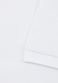 Biała dzianina z delikatnym ściągaczem i wytłoczonymi literami "P.L." w dopasowanym białym odcieniu. Miękka tekstura, minimalny design.