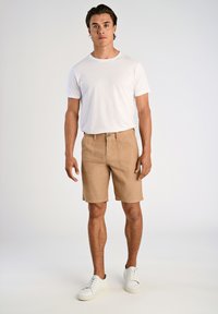 Beiga, strukturerade shorts med framfickor och knappstängning, i kombination med en vit t-shirt med rund halsringning och vita sneakers. Neutrala färger.