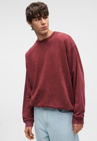 Μακρυμάνικο φούτερ σε χρώμα μαρόν, μείγμα βαμβακιού, χαλαρή εφαρμογή, στρογγυλή λαιμόκοψη, χαμηλωμένοι ώμοι, ριμπ μανσέτες, συνδυασμένο με ανοιχτό μπλε τζιν.