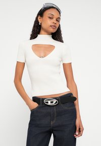 Λευκή ριμπ πλεκτή μπλούζα με κοντά μανίκια, ψηλό λαιμό και καρδιοειδές άνοιγμα με μεταλλική λεπτομέρεια. Συνδυάζεται με μαύρο τζιν σκουρόχρωμο και μαύρη ζώνη.