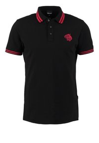 Polo noir à manches courtes avec des rayures rouges sur le col et les poignets et une tête de tigre rouge brodée sur la poitrine gauche.