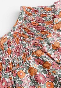 Kwiatowy materiał z marszczonym dekoltem w odcieniach różu, pomarańczy i zieleni. Posiada małe kwiaty na białym tle.