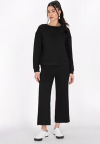 Outfit composto da felpa nera con texture e pantaloni a gamba larga, abbinato a sneakers bianche; presenta un collo tondo e una vestibilità comoda.