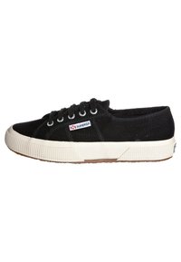 Sneaker nera in tela con suola in gomma bianca, dotata di lacci tondi e un motivo testurizzato sui lati. Include una piccola etichetta logata in rosso e blu.
