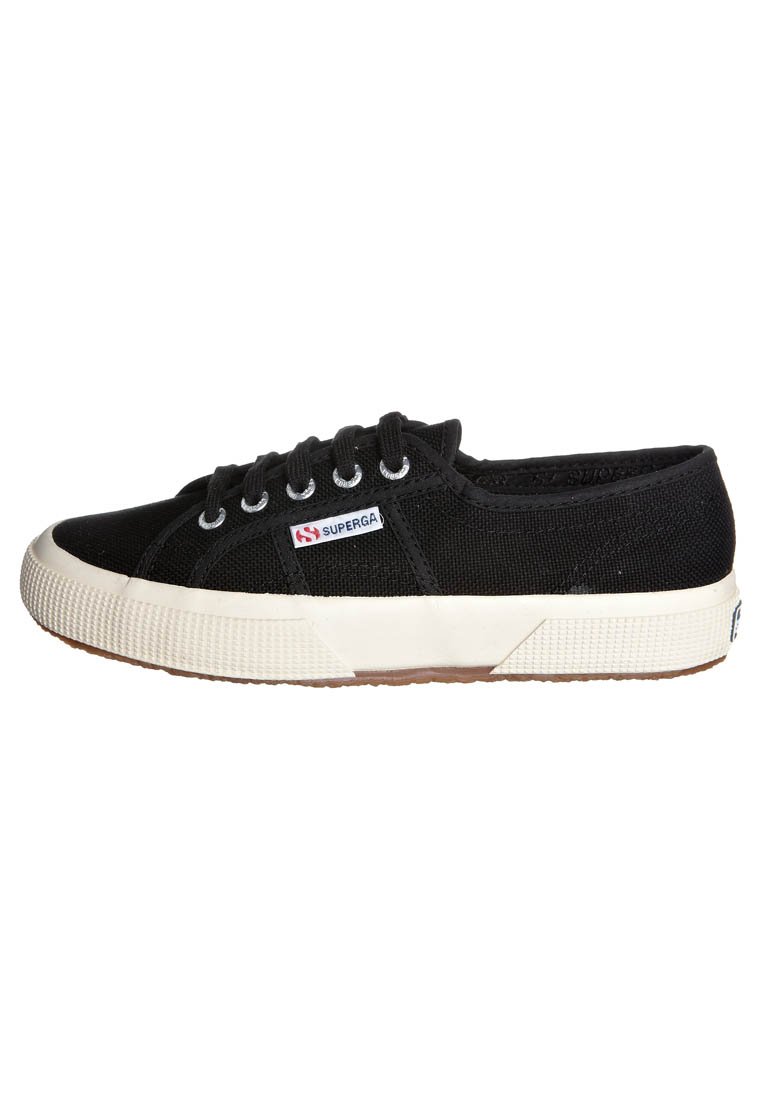Sneaker nera in tela con suola in gomma bianca, dotata di lacci tondi e un motivo testurizzato sui lati. Include una piccola etichetta logata in rosso e blu.