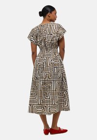 Robe en coton à coupe décontractée, dotée d'un motif géométrique abstrait marron et noir sur fond crème, avec une taille cintrée et des manches courtes.