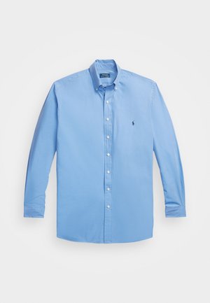 Camisa azul clara de manga longa, com colarinho clássico e pequeno logotipo bordado no peito, feita de um material de algodão suave.