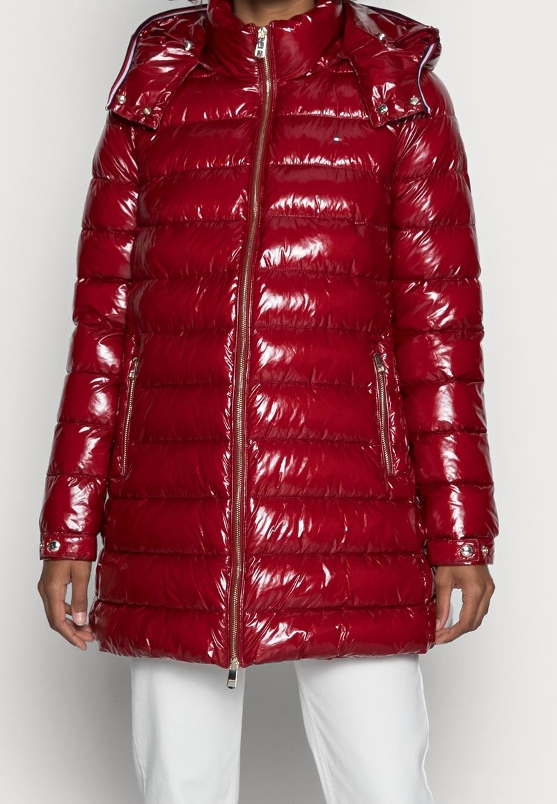 Red padded puffer coat with a glossy finish, zip closure, side pockets, and a detachable hood. Features horizontal quilting and silver accents.