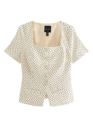 Blusa de manga corta color crema con lunares negros, escote cuadrado, botones delanteros y dos pequeños bolsillos en la cintura.