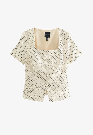 Blusa de manga corta color crema con lunares negros, escote cuadrado, botones delanteros y dos pequeños bolsillos en la cintura.
