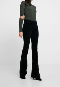 Pantalon évasé en velours côtelé noir associé à un haut à manches longues côtelé vert foncé, avec une silhouette ajustée et un col haut.