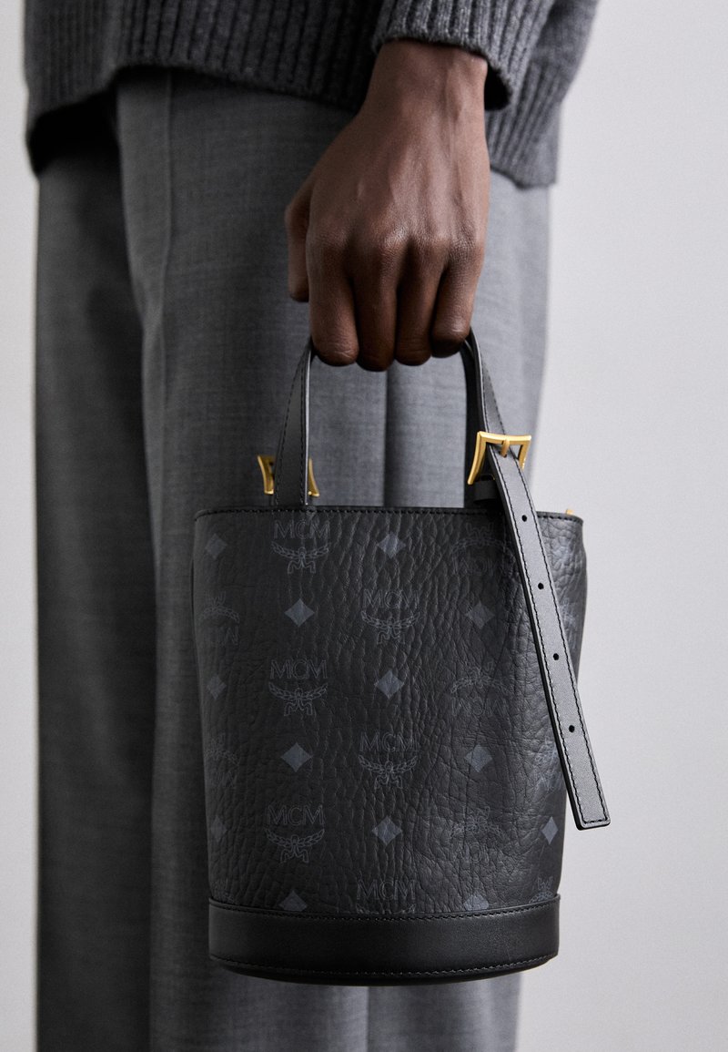 Sac seau en cuir noir avec motif de logo embossé, quincaillerie dorée, doubles poignées et bandoulière amovible. Design structuré.