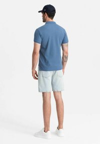 Ljusblå pikétröja, kort ärm, i bomullsmaterial; kombinerad med ljusa denimshorts och vita sneakers; bär en marinblå keps.