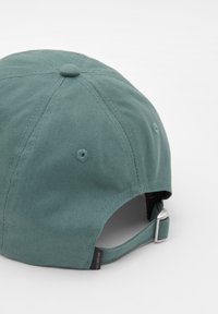 Zöld, pamut baseballsapka kerek koronával, hátul állítható pánttal és varrási részletekkel. Szellőzőlyukakkal és címkével rendelkezik.