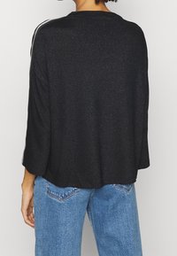 Svart, texturerad tröja med trekvartsärmar och lös passform. Har en subtil lyster och kontrasterande silverränder på axlarna.