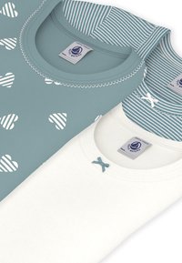 Deux hauts à manches courtes : un bleu sarcelle avec des motifs de cœurs blancs et un haut blanc avec un nœud bleu sarcelle. Les deux présentent des encolures arrondies et des détails cousus.