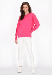 Felpa rosa con maniche lunghe e spacchi laterali, abbinata a jeans skinny bianchi e sneakers bianche. Texture liscia e vestibilità comoda.