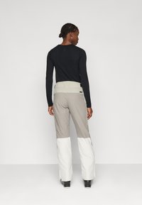 Ski pants in beige and white, with a high waistband and zipper details. Soft, stretchy fabric designed for movement and comfort.